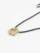 Collar con cordón negro y dije circular dorado con textura irregular.