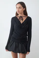 Top de manga larga color negro, con escote drapeado y detalle de tiras finas para anudar en el cuello. Confeccionado en tejido elástico y suave.