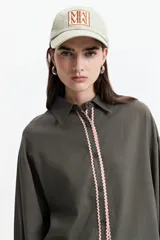 Camisa oversize color verde militar con botones frontales y detalle de volados rosas en el borde de la botonadura.