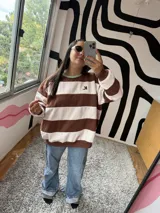 Buzo de corte holgado con diseño de rayas horizontales anchas en color chocolate y crudo. Presenta cuello redondo en color verde menta y puños elásticos.