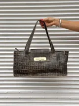 Cartera tipo tote bag de diseño rectangular y alargado, con acabado texturizado efecto piel de cocodrilo en tonos marrones y desgastados. Presenta una solapa frontal con cierre metálico dorado y doble asa de hombro.