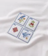 Remera de algodón marca Marfinno, color blanco, con cuello redondo y detalle de ribete en contraste. Presenta un diseño de cuatro sellos bordados en el pecho.