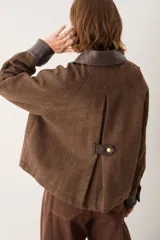 Campera de paño en color azul oscuro, con cuello, puños y bolsillos frontales en cuero sintético color verde. Presenta cierre frontal con botones dorados.