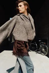Jersey de punto con cuello subido y mangas largas acampanadas. Presenta un diseño envolvente con detalle de bufanda integrada en el mismo tejido y textura jaspeada.