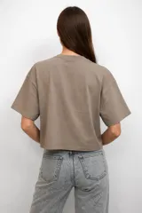 Remera de algodón color gris topo, de corte holgado y diseño cropped. Presenta cuello redondo y una estampa frontal con forma de corazón, mariposa y texto decorativo.