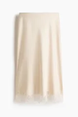 Pollera midi de satén color beige con leve brillo, corte recto y detalle de encaje festoneado en el borde inferior.