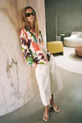 Camisa satinada de manga larga con cuello solapa y cierre frontal con botones, con un colorido estampado floral de estilo acuarela sobre fondo beige.