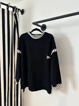 Buzo oversize de color negro con detalles de rayas blancas y negras en el cuello, puños y hombros. Presenta un pequeño parche bordado en el pecho.
