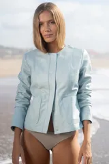 Campera de cuero ovino color celeste claro, estilo chaqueta corta, con cuello redondo y cierre frontal de botones. Presenta bolsillos delanteros con solapa curva.