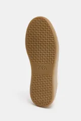Zapatilla tipo bamba con diseño de paneles en combinación de colores y materiales, incluyendo detalles en cuero sintético y gamuza. Presenta suela de plataforma en contraste y cierre mediante cordones.