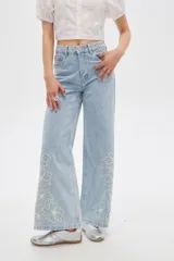 Pantalón jean de tiro alto y corte ancho, color celeste, con delicados bordados de flores blancas en la parte inferior de las piernas.