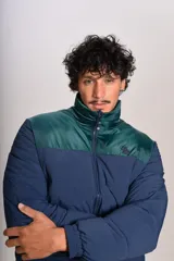 Campera puffer con diseño bicolor, cuerpo en azul marino y canesú superior en verde oscuro. Presenta cuello alto, cierre frontal completo y puños elásticos.