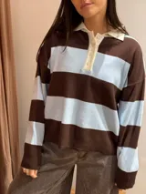 Sweater tipo chomba de tejido bremer con diseño de rayas horizontales en color marrón y celeste. Presenta cuello polo en color crema con cierre frontal de botones y mangas largas.