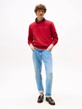 Buzo rojo de cuello redondo con ribetes distintivos, logo texturizado de Tommy Hilfiger en el pecho y logo bordado en la manga. El cuello es azul marino y se asoma un cuello de camisa a rayas. Los puños tienen ribetes distintivos.