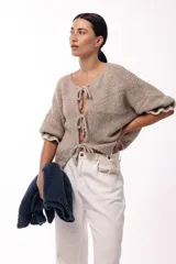 Saco de punto gris con frente abierto, cierre mediante lazos frontales y mangas con puños elásticos. Presenta una textura suave y un diseño de volumen holgado.