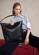 Bolso tipo shopper de cuero vacuno, color negro, con diseño minimalista, costura central vertical y asa de hombro ajustable con hebilla metálica.