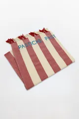 Pareo-lona rectangular con rayas horizontales rojas y blancas, con flecos en los extremos y la palabra "PASTICHE" bordada en azul.