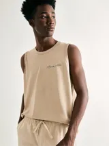 Musculosa de algodón color beige con cuello redondo y estampa pequeña en el pecho con texto y diseño lineal.