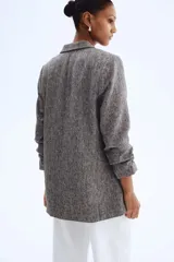 Blazer largo de corte recto con solapas de muesca, cierre frontal de un botón y bolsillos delanteros ribeteados. Presenta hombreras, pinzas en la cintura y mangas tres cuartos con diseño fruncido. Incluye forro interior.