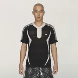 Remera de punto Adidas Originals by Edison Chen CLOT Knit Jersey, color negro con detalles en beige, cuello en V con cierre frontal y las icónicas tres tiras en las mangas.
