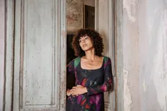 Vestido corto de mangas largas con estampado abstracto en tonos violeta, verde y rojo sobre fondo negro.