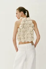 Top corto de cuello halter, confeccionado con una estructura de tejido que forma flores en relieve por toda la prenda. Presenta cierre en la espalda con abertura y botón oculto.