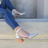 Sandalias de cuero color beige con textura sutil en la puntera afilada, taco cuadrado de madera de 6.6 cm y tira al tobillo con hebilla metálica.