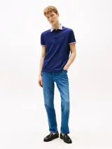 Chomba azul marino de algodón elástico, con cuello tejido a contraste en blanco y gris con ribete naranja. Tiene tapeta de dos botones, mangas cortas con ribete a contraste y logo de Tommy Hilfiger bordado en el pecho.