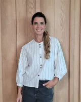 Camisa de corte recto con estampado de rayas verticales finas, cuello redondo y cierre frontal con botones. Presenta mangas largas abullonadas con puños elásticos.