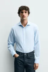Camisa de corte regular fit confeccionada en tejido de algodón con textura. Presenta cuello italiano, manga larga con puños abotonados y cierre frontal de botones.