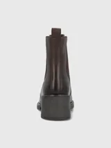 Bota tipo botín de cuero color marrón oscuro, con elásticos laterales y detalles de tachas metálicas doradas a lo largo de la caña. Cuenta con suela gruesa y taco cuadrado de altura media.