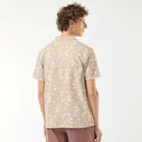 Remera polo de piqué color beige con estampado de palmeras y motivos playeros en blanco.