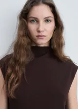Vestido midi de color marrón chocolate, con cuello perkins, diseño sin mangas y corte evasé. Presenta un bajo asimétrico y cierre de botón en la parte posterior.