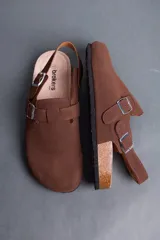Sandalias marrones estilo zueco de hombre, con tira ajustable en el empeine y en el talón con hebillas metálicas. Presentan suela de corcho y base de goma estriada.