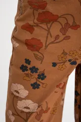 Jean de corte baggy y tiro medio, confeccionado en algodón peinado. Presenta un diseño estampado con motivos florales en tonos tierra sobre una base color marrón.