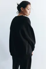 Buzo negro liso, de corte oversized con cuello redondo y hombros caídos. Presenta puños y bajo acanalados.