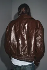 Chaqueta de Zara Woman Collection en tejido con acabado brillante efecto cuero. Presenta cuello solapa, manga larga con trabillas ajustables, bolsillos delanteros y cierre frontal con botones ocultos bajo solapa.