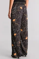 Pantalón pijamero de satén texturado color negro con estampado de flores amarillas y líneas blancas. Tiene calce relajado, cintura elastizada y bolsillos ocultos.