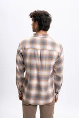 Camisa de manga larga con estampado de cuadros en tonos gris, beige y blanco. Presenta cuello abotonado, cierre frontal con botones y un bolsillo en el pecho.