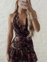 Vestido corto con estampado abstracto en tonos marrones y verdes, diseño halter con escote profundo y detalle de volado en el ruedo. Incluye una cadena metálica plateada a modo de cinturón.