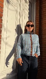 Cardigan reversible de punto con estampado de rombos pequeños, cuello alto y cierre frontal completo con botones. Presenta detalles de ribetes en color contrastante en cuello, puños y cartera de botones.