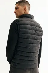 Chaleco acolchado de nylon rompevientos, color negro, con diseño guateado, cuello elevado y cierre frontal. Cuenta con bolsillos laterales con cierre y forro interior.