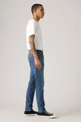 Pantalón de jean corte slim taper, con diseño de cinco bolsillos, cierre de cremallera y botón metálico, en tono azul medio con efecto lavado.