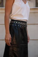 Pollera larga de ecocuero negro, de corte recto y tiro medio-alto. Presenta una cintura decorada con una hilera de ojales metálicos plateados.
