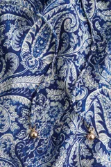 Vestido evasé corto con escote amplio de volados y elástico revestido, estampado con diseño paisley en tonos azul y blanco. Cuenta con abertura en V con tiras finas para atar y cuentas decorativas, además de mangas globo cortas con forro.
