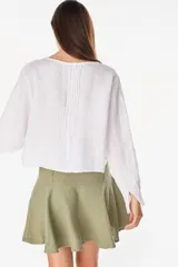 Camisa blanca de lino italiano, de manga larga, escote en V y cierre frontal con múltiples botones y detalles de alforzas.