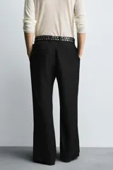 Pantalón de vestir gris oscuro, corte ancho (flare fit) y tiro alto, con bolsillos laterales y falsos bolsillos de vivo en la parte trasera. Presenta un cierre frontal con cremallera y gancho oculto, y botones a presión ocultos en el bajo.