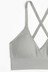 Top deportivo gris con breteles finos cruzados en la espalda, confeccionado en tejido funcional DryMove™ que ayuda a absorber el sudor. Tiene copas forradas con relleno extraíble y elástico ancho en el bajo.