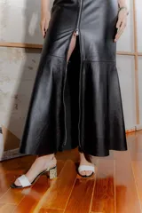 Vestido largo negro de cuero ovino con cierre frontal de cremallera metálica, sin mangas y con tajo lateral.