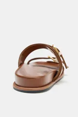 Sandalia plana color marrón con tiras de tela color crudo y hebillas doradas.